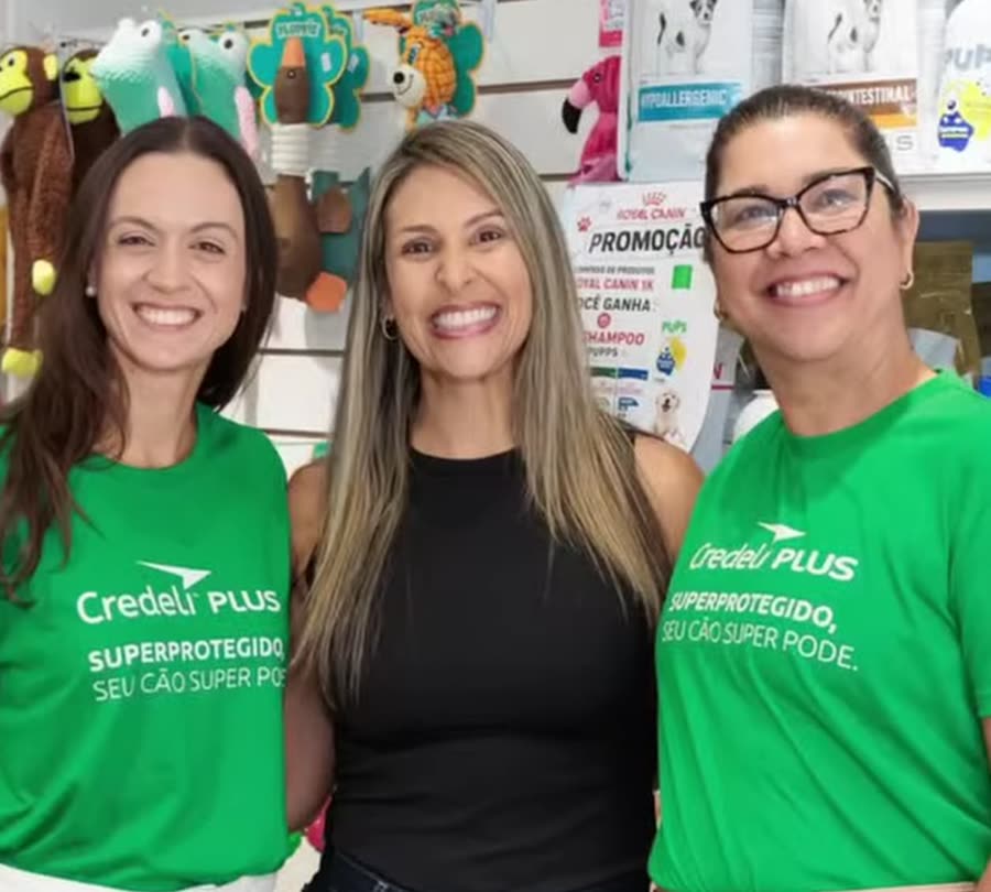 As três atendentes da Pet a Pet sorrindo dentro da loja, com as prateleiras de brinquedos ao fundo